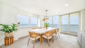 A dining area with a white table, wooden chairs, and potted plants. - Shores Club 801 - Oceanfront Modern Luxury (Daytona Beach Shores)