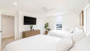 A modern bedroom with two beds, a TV, a ceiling fan, and a view of the sea. - Shores Club 801 - Oceanfront Modern Luxury (Daytona Beach Shores)
