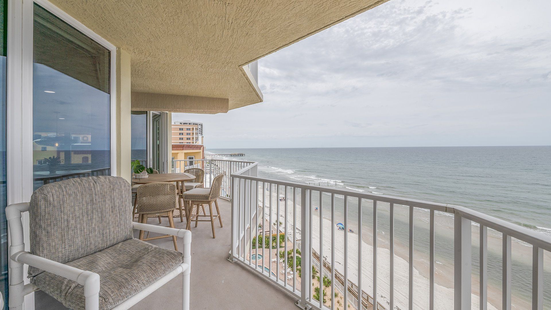 A balcony with a view of the ocean, a dining area with wicker furniture, and a pool area.