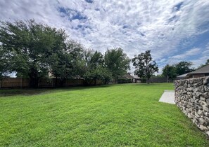 A backyard with a stone wall, a grassy lawn, and trees.