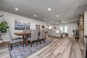 A spacious living area with a dining table, chairs, a sofa, and a kitchen in the background.