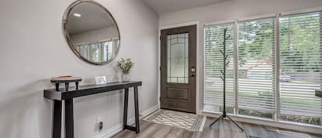 A modern entryway with a dark console table, a round mirror, a potted plant, a door with frosted glass panels, and a large window with blinds.