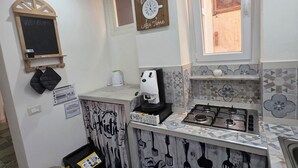 A compact kitchen with a coffee machine, a stove, and a clock on the wall.