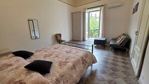 A bedroom with a bed, a chair, a sofa, a window, and a door.