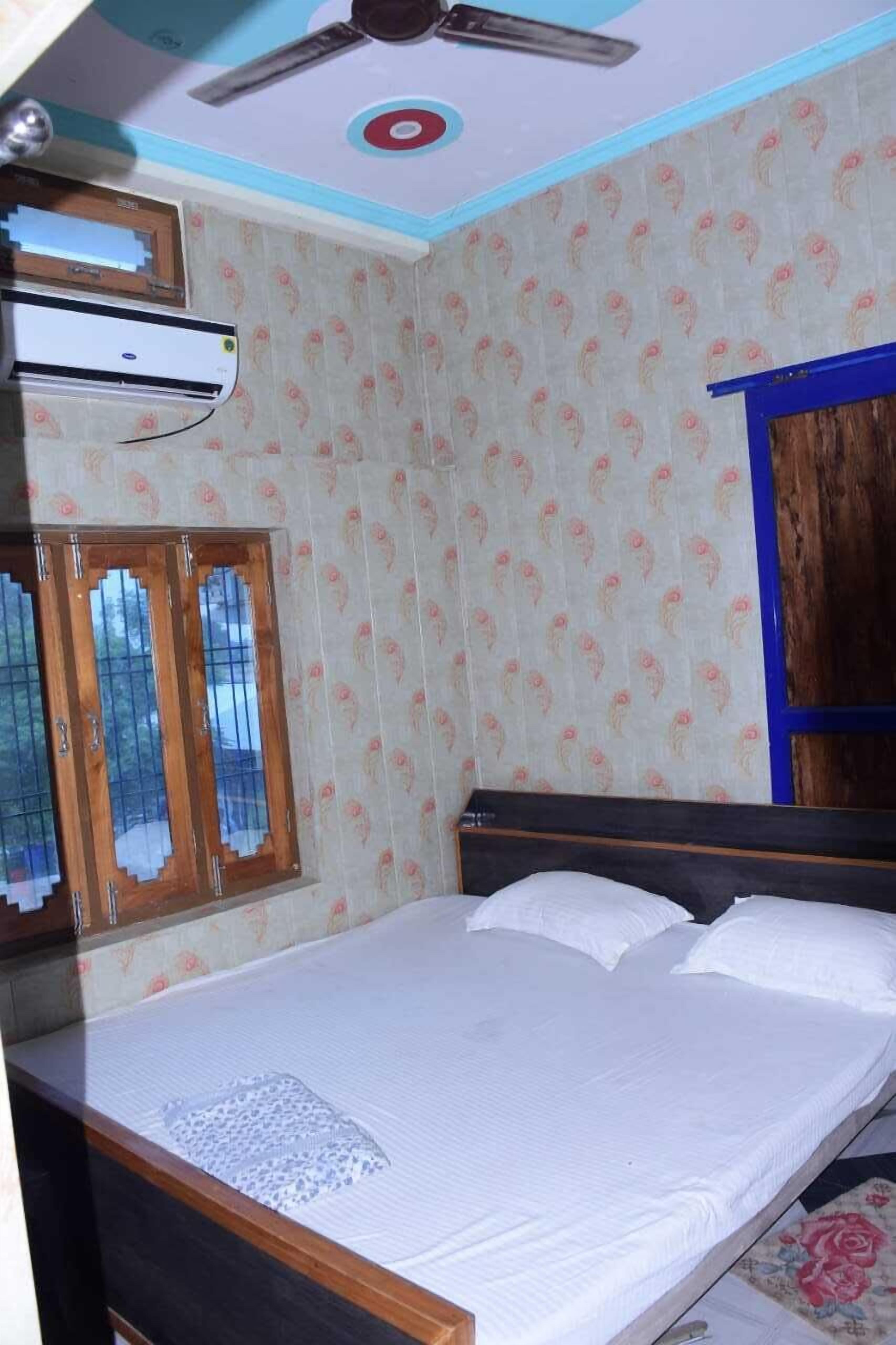 A bedroom with a bed, an air conditioner, a ceiling fan, and a window with a wooden frame.
