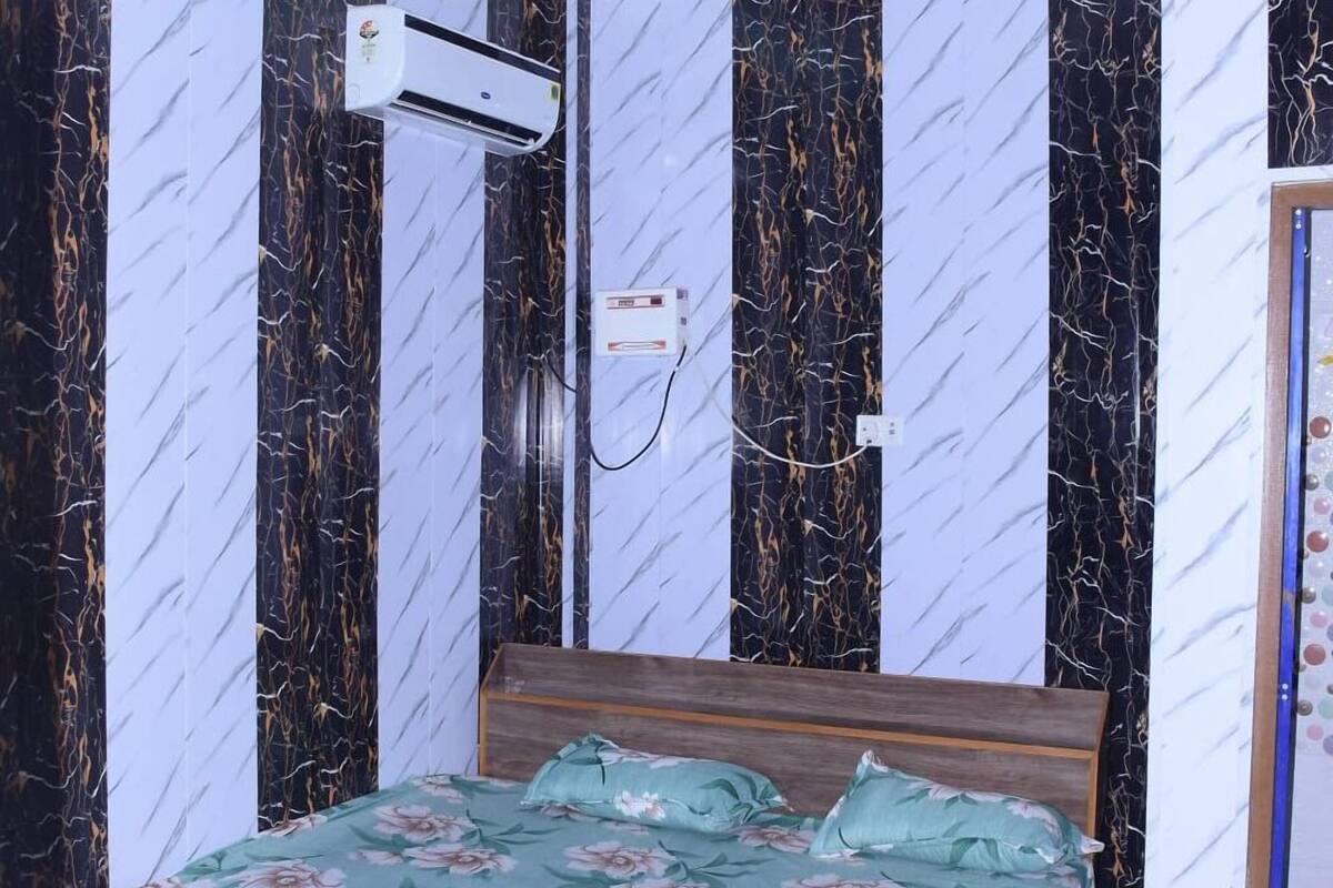 A bedroom with a bed, air conditioning unit, and patterned walls.