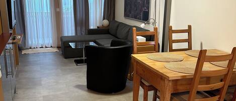 A modern living room with a sofa, a dining table with chairs, and a cityscape painting on the wall.