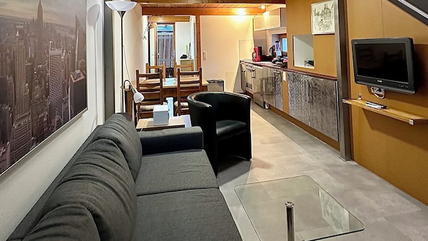 Una sala de estar moderna con un sofá, una mesa de centro de vidrio y un televisor montado en la pared.