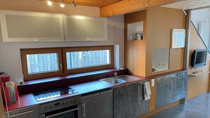 Una cocina compacta con horno empotrado, un lavamanos y una ventana con persianas de madera.