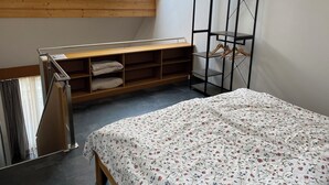 Un dormitorio con tragaluz, un banco de madera, un armario de metal negro y una cama con colcha estampada.