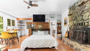 Un dormitorio con cama, chimenea de piedra, televisor y comedor con sillas y mesa.