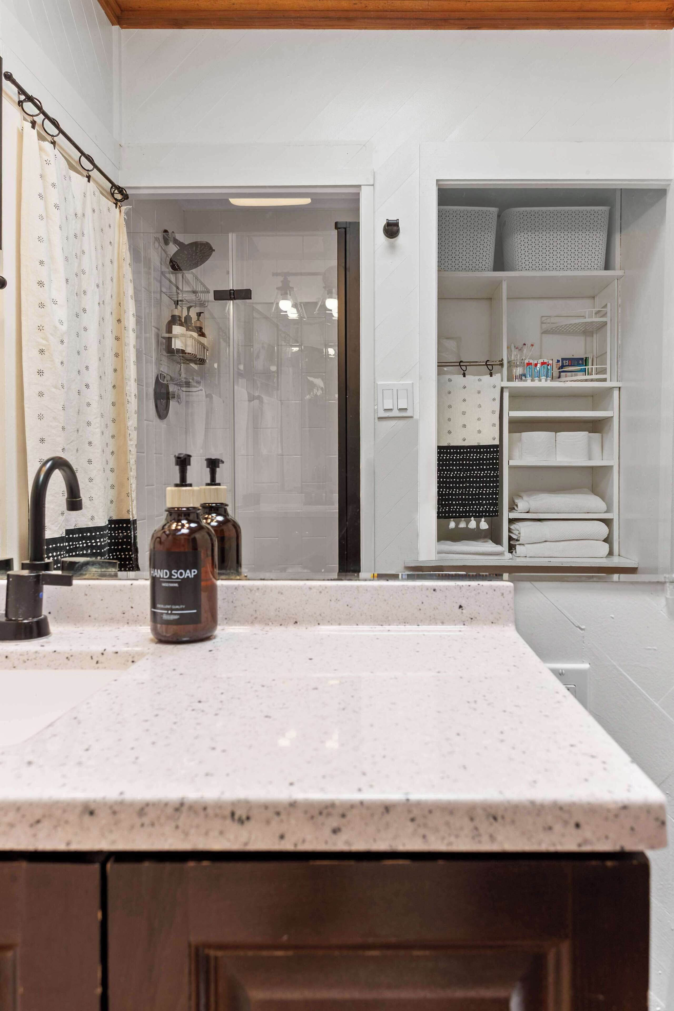 Een badkamer met een wastafel, handzeep, een douche en een opbergkast.