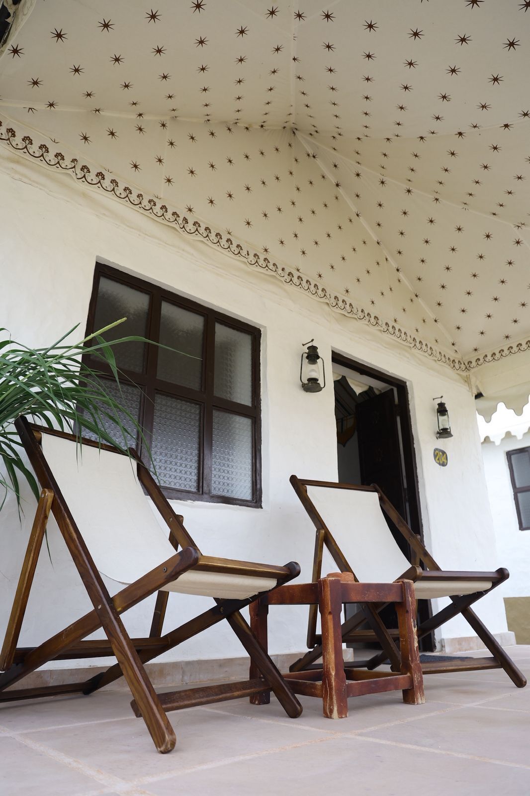 Ein überdachter Sitzbereich im Freien mit zwei Holzstühlen und einem Blumentopf.
