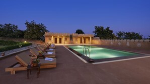 A poolside area with lounge chairs and a swimming pool, surrounded by a low wall and trees. - Hariyali Dhani Camps & Desert Resort With Swimming Pool, Jodhpur (Dheerpura)