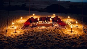 A desert camp with a central seating area surrounded by candles, set against a backdrop of sand dunes and a twilight sky. - Hariyali Dhani Camps & Desert Resort With Swimming Pool, Jodhpur (Dheerpura)
