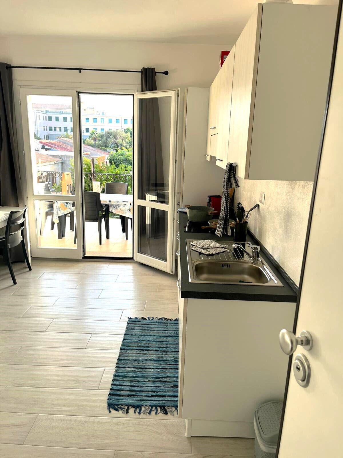 Une cuisine compacte équipée d’un évier, de placards et offrant une vue sur le balcon extérieur.
