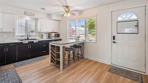 A modern kitchen with a central island, black bar stools, and a ceiling fan. - The Big Muddy Riverfront Bungalow (Princeton)