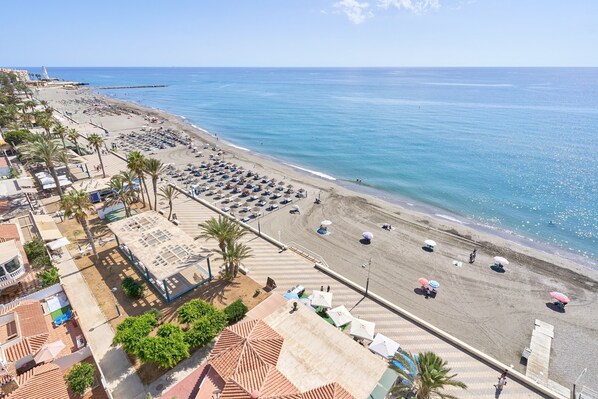 Un hotel frente a la playa con estacionamiento, sombrillas y vista al mar.