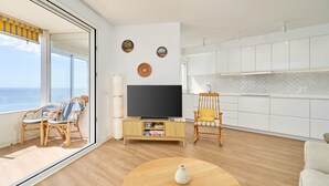 Un salon moderne doté d’un grand téléviseur, de fauteuils en osier, d’une table basse ronde et offrant une vue sur l’océan.