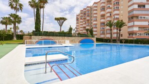 Une piscine avec un plongeoir, des palmiers et un immeuble à plusieurs étages en arrière-plan.