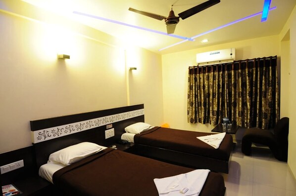 A hotel room with two beds, a ceiling fan, an air conditioning unit, and a window with curtains. - hotel skylawn surat (Surat)