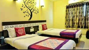 Habitación de hotel con dos camas, un mural decorativo de un árbol en la pared, un equipo de aire acondicionado y cortinas estampadas.