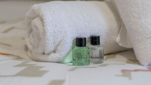 Un asciugamano bianco piegato ordinatamente su un letto, con due piccole bottiglie di liquidi, probabilmente articoli da toilette, accanto.