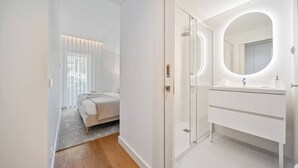 A modern bedroom with a large bed, a walk-in closet, and a bathroom with a large mirror and white fixtures. - To complete (Funchal)