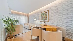 A modern living room with a wooden dining table, white sofas, and a large potted plant. - To complete (Funchal)