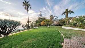 Una zona enjardinada i ben cuidada amb palmeres i un camí pavimentat.