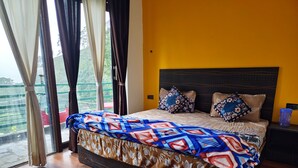 Een slaapkamer met een bed, een nachtkastje, een raam met gordijnen en uitzicht op groen.