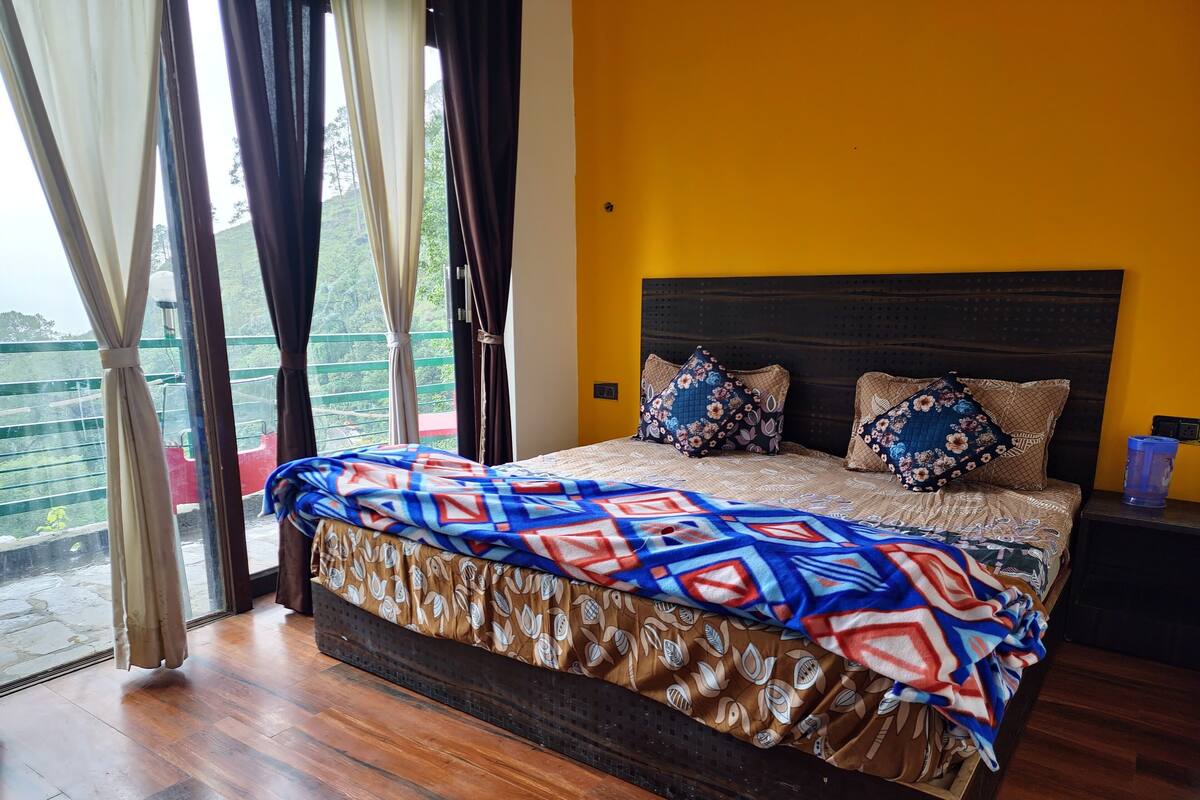 A bedroom with a bed, a nightstand, a window with curtains, and a view of greenery outside.