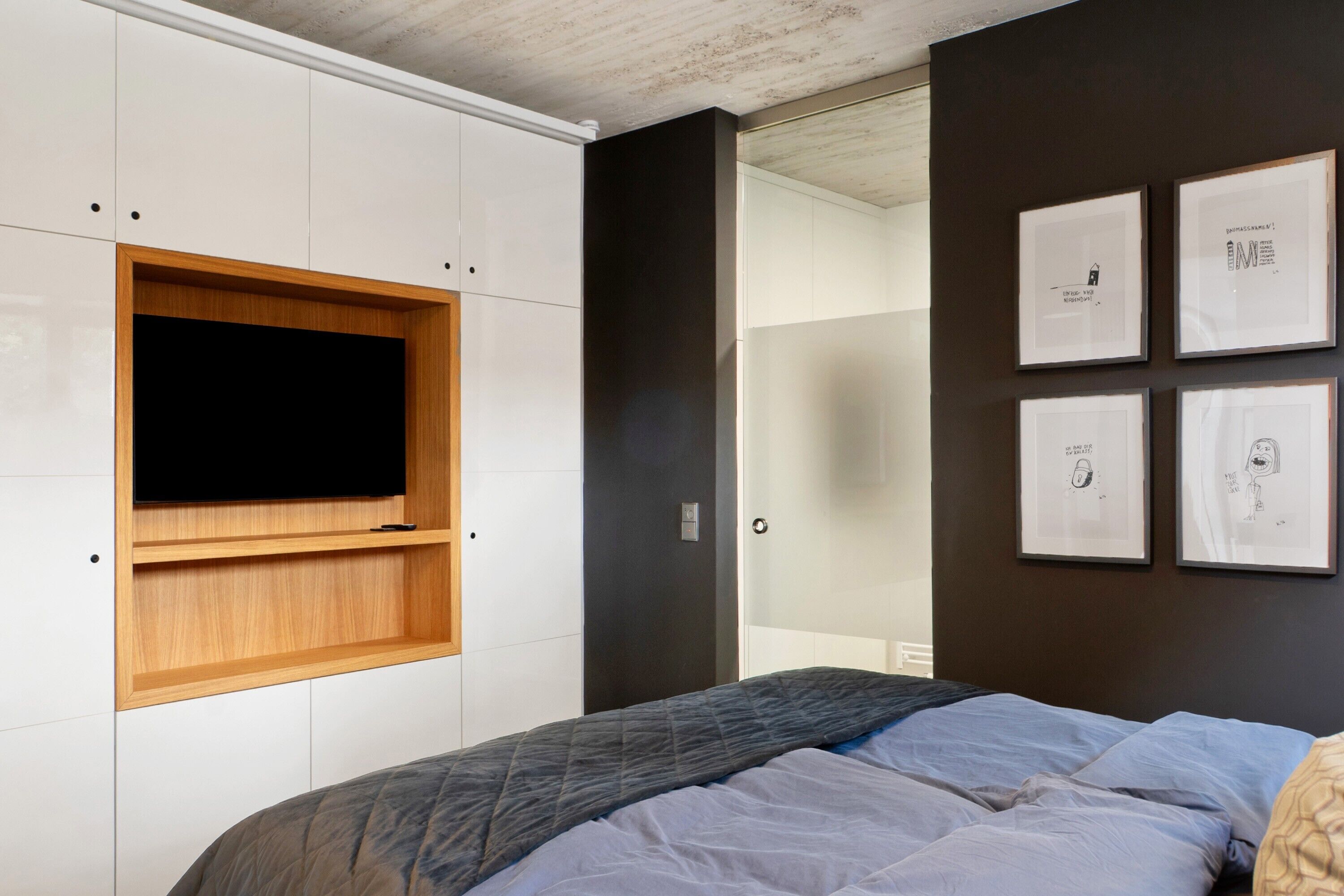 A bedroom with a bed, a TV mounted on a white cabinet, and framed artwork on the wall.