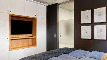 A bedroom with a bed, a TV mounted on a white cabinet, and framed artwork on the wall.