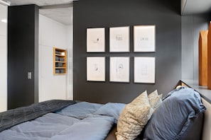 Ein Schlafzimmer mit einem Bett, Kissen, einem Wandregal und gerahmten Kunstwerken.