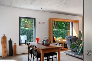 Ein modernes Interieur mit Essbereich, einer Couch und großen Fenstern mit Blick ins Grüne.