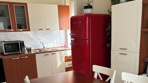 Une cuisine avec une table en bois, des chaises blanches, un réfrigérateur rouge et des placards.