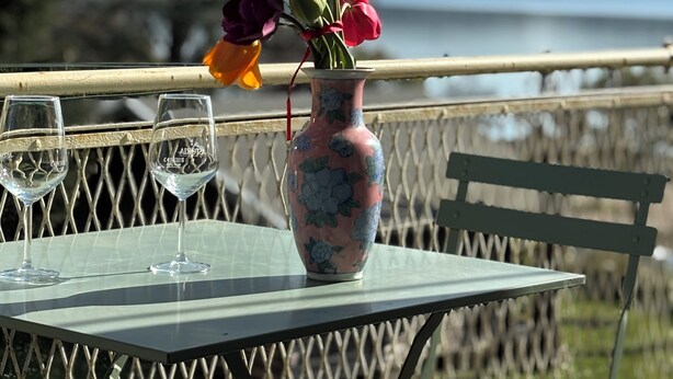 Une table sur laquelle se trouve un vase de fleurs et deux verres, le tout posé sur une table en métal. En arrière-plan, on aperçoit un lac et des collines.