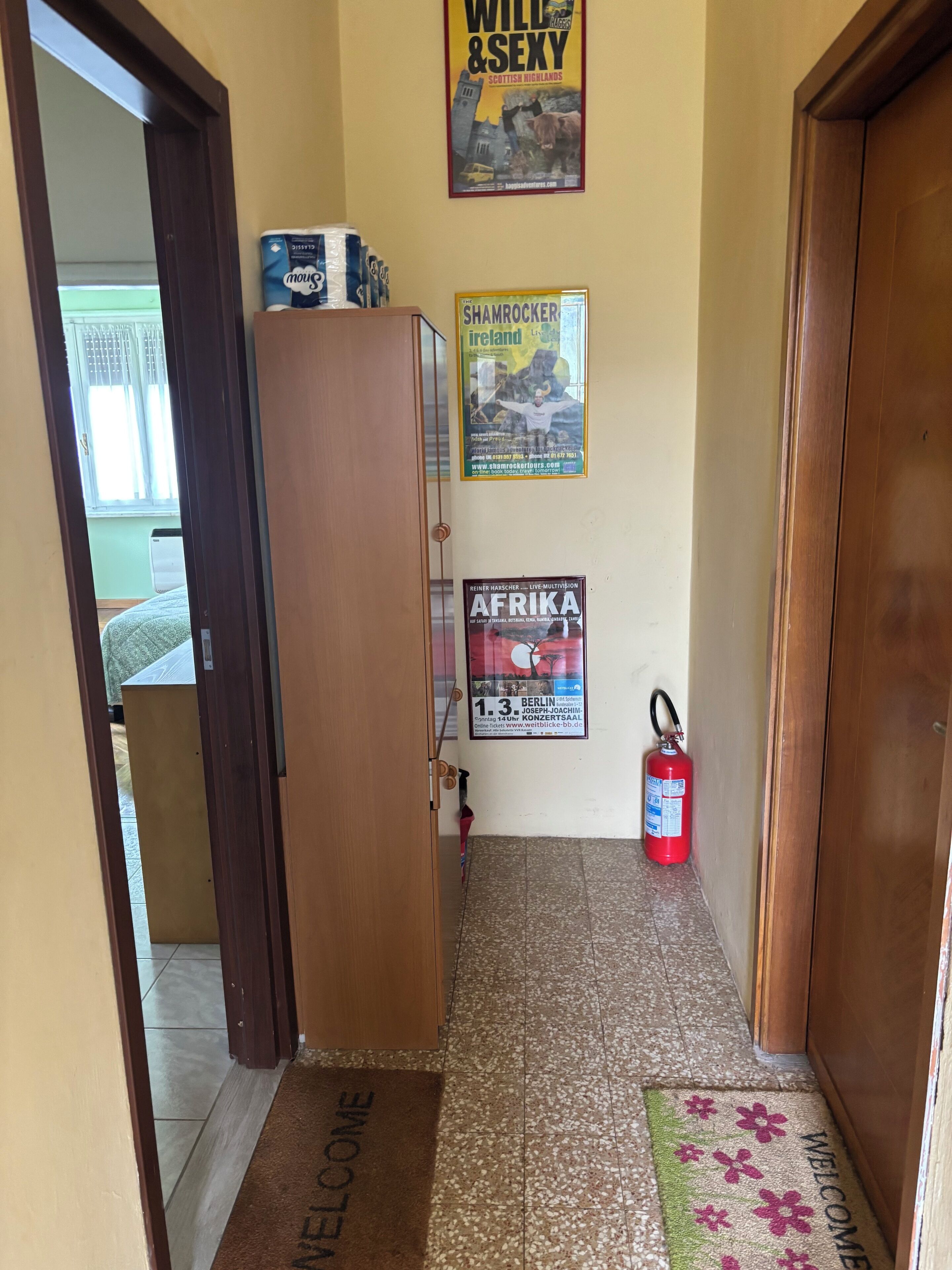 Een gang met een houten deur, een brandblusser en een welkomstmat.