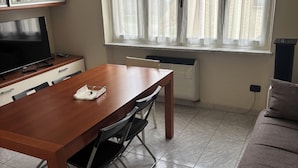 Un salon comprenant une table à manger en bois, des chaises, un canapé, un téléviseur et une fenêtre avec des rideaux.