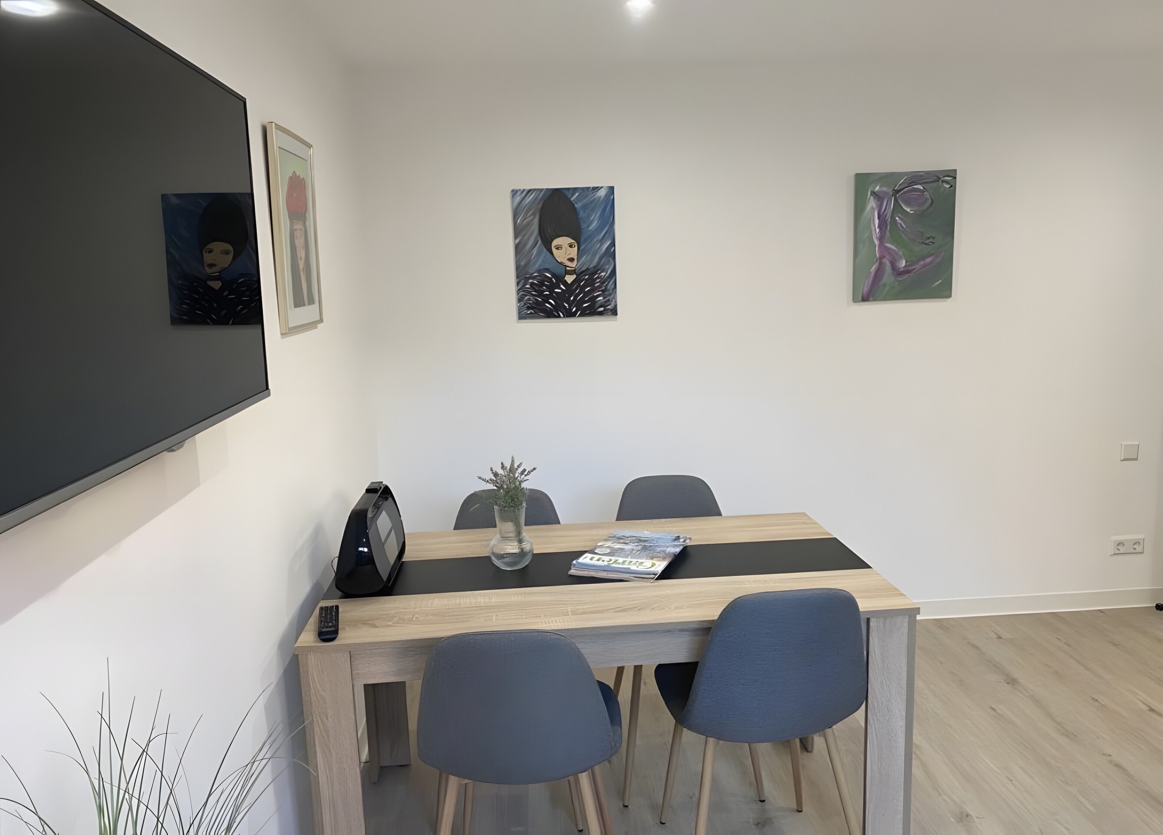 A conference room with a large flat-screen TV, a wooden table, two chairs, and three framed artworks on the wall.