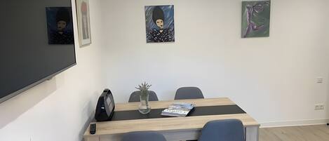A conference room with a large flat-screen TV, a wooden table, two chairs, and three framed artworks on the wall.