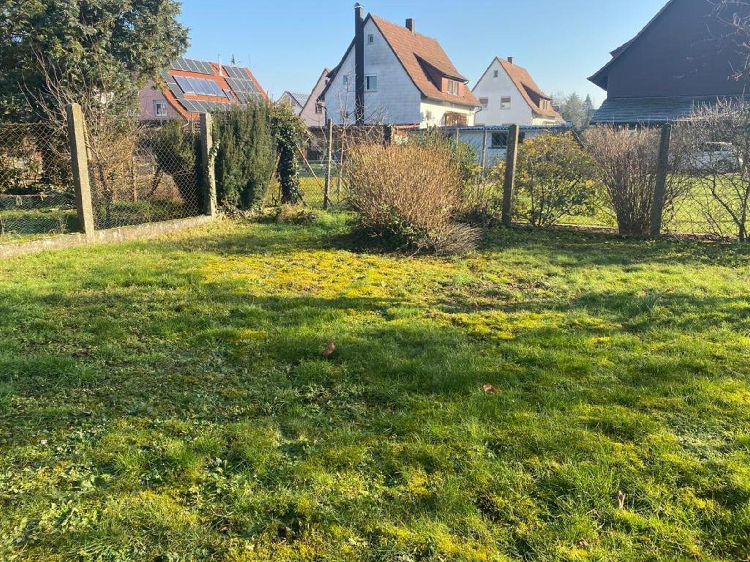 A grassy area with a fence, trees, and houses in the background.