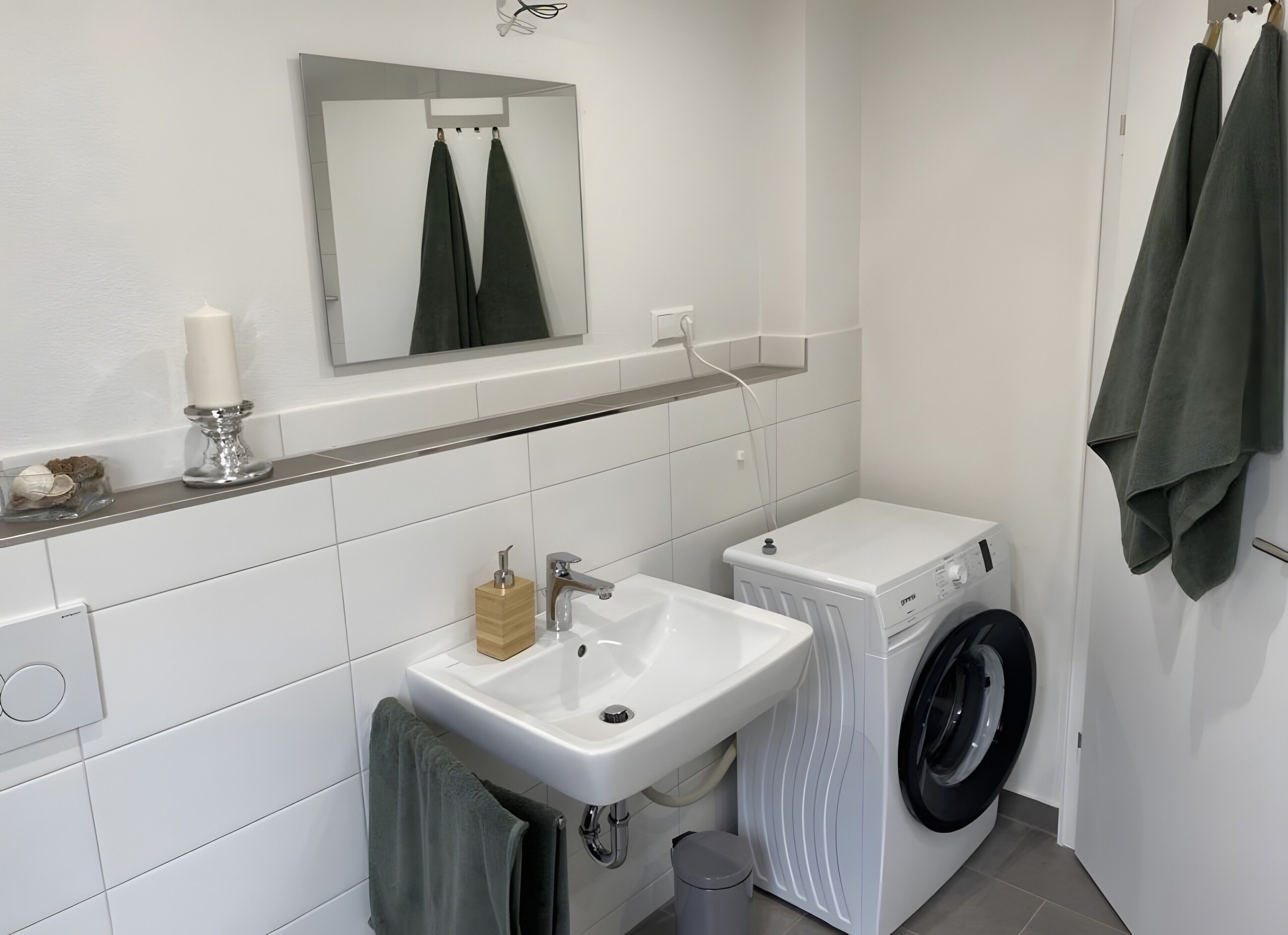 A bathroom with a sink, mirror, towel rack, and a washing machine.