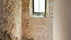 Una escalera de paredes de piedra con un pequeño ventanal en la parte superior, una escultura decorativa de cuerda y una pequeña figurina en el rellano.