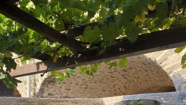 Un área de piscina con paredes de piedra, una pérgola en lo alto, una pared de piedra con una ventana y un banco de piedra.