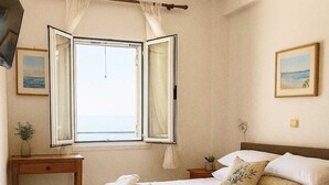 A bedroom with a bed, a bedside table, a nightstand, a window with curtains, and a ceiling light. - Beachfront Panorama Aprtmnt - Kythira Seafront Gem (Kithira)