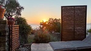 Eine Terrasse mit Blick auf den Sonnenuntergang über dem Meer, ein Korbsichtschutz und eine Backsteinmauer mit einem Blumentopf.
