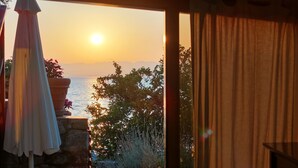 Ein Zimmer mit Meerblick bei Sonnenuntergang, einer Zimmerpflanze und einem Vorhang.