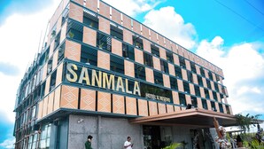 A hotel named SANMALA with a modern design, featuring a prominent entrance and a covered outdoor area with potted plants.